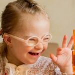 Smiling young child with glasses playing with blocks, illustrating inclusive, sensory‑friendly pediatric dental care.