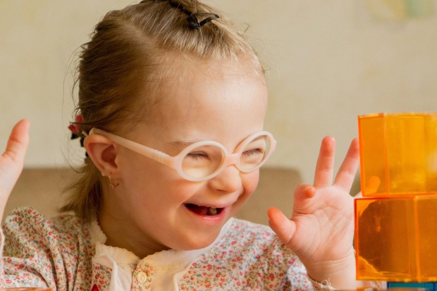 Smiling young child with glasses playing with blocks, illustrating inclusive, sensory‑friendly pediatric dental care.