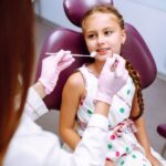 Young girl receiving dental examination in pediatric dentist office with purple chair.