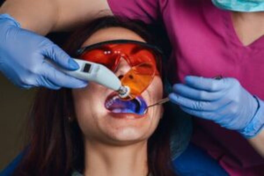 Pediatric dentist examines child's teeth with orange-tinted glasses and dental tool during examination.