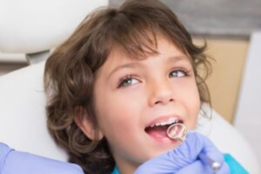Young child receiving dental examination from dentist wearing blue gloves in clinical setting.