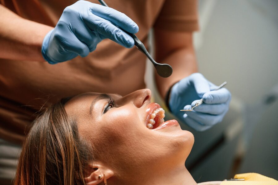 Pediatric dentist examining young patient's teeth with dental mirror and tools during checkup.