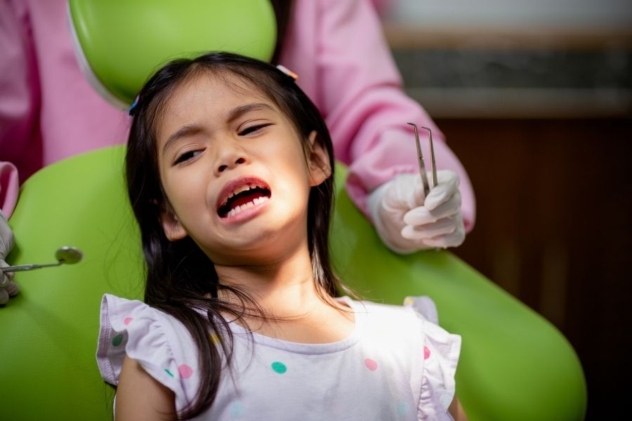 Young girl receiving dental examination in pediatric dentist's chair with dentist in pink attire.