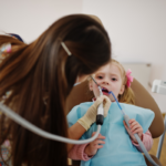 Young patient receiving dental examination with suction tool in dental chair.