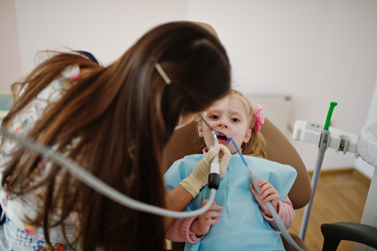 Young patient receiving dental examination with suction tool in dental chair.